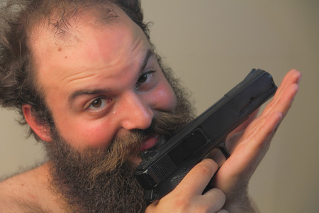 29581457-a-balding-bearded-man-mugs-for-the-camera-while-displaying-his-pistol.jpg