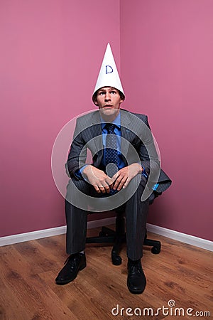 businessman-sat-corner-wearing-dunce-hat-10187379.jpg