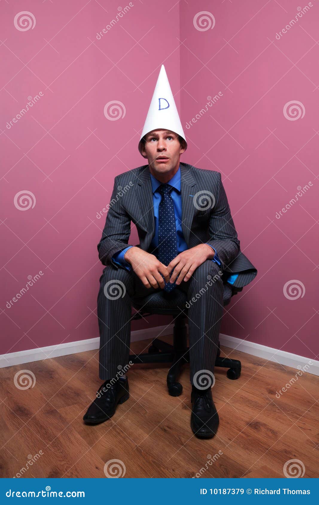businessman-sat-corner-wearing-dunce-hat-10187379.jpg