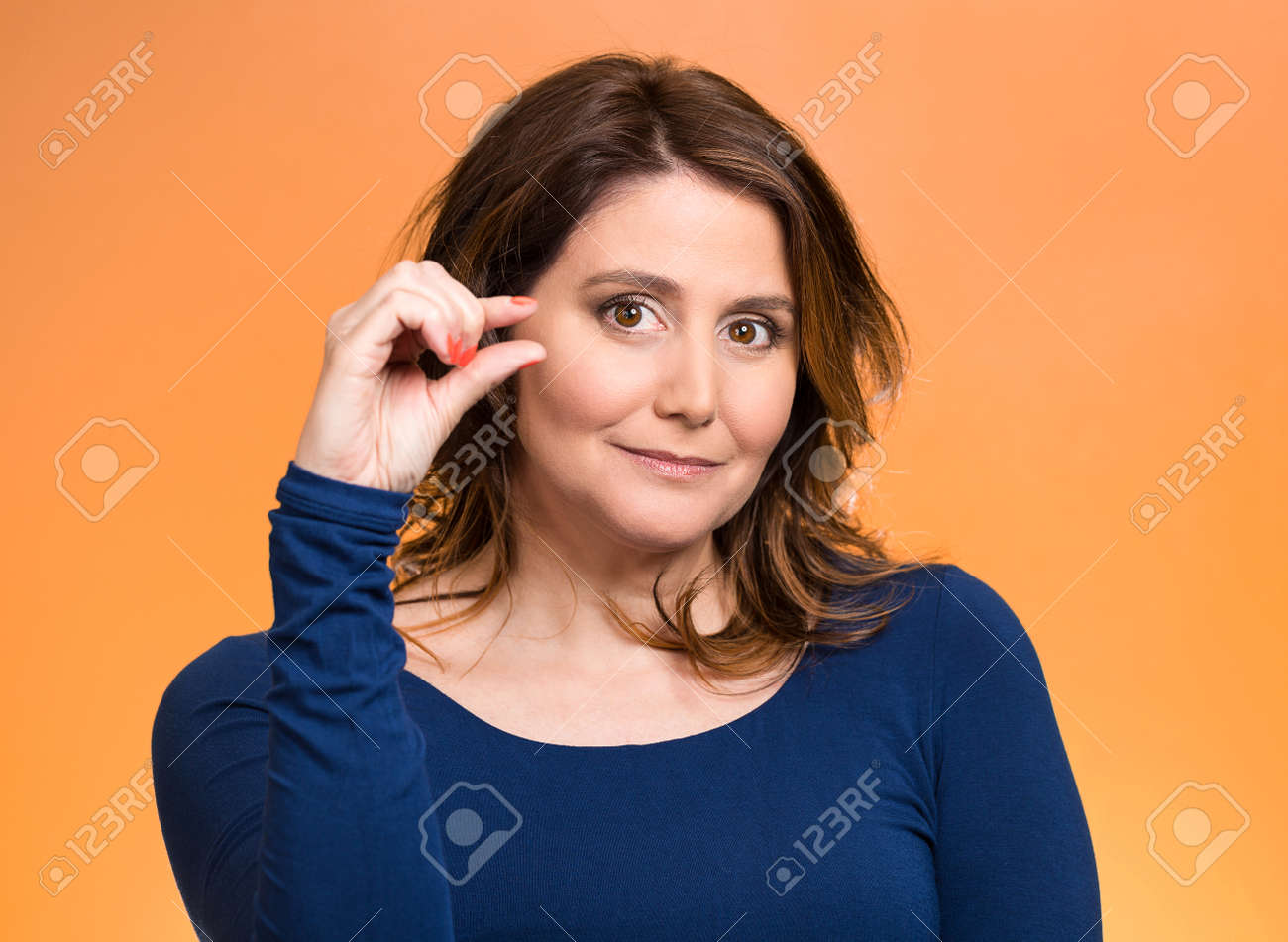 31160087-Closeup-portrait-young-middle-aged-woman-showing-small-amount-gesture-with-hands-isolated-orange-bac-Stock-Photo.jpg