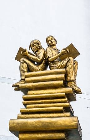 19899492-golden-statue-boy-and-girl-sitting-on-book-at-white-concrete-backgrounds.jpg